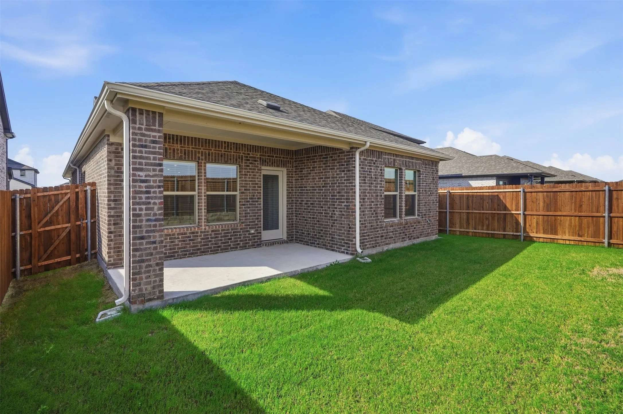 Expansive green lawn, covered patio, brick exterior, wood privacy fencing, and a shingled roof