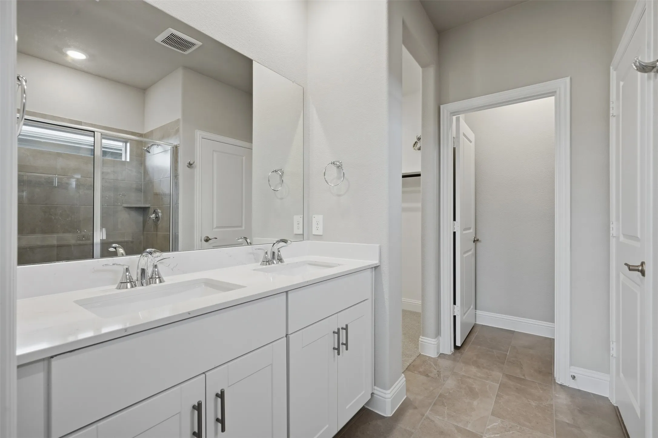 Dual vanity with white cabinetry, polished chrome fixtures, and a large integrated mirror