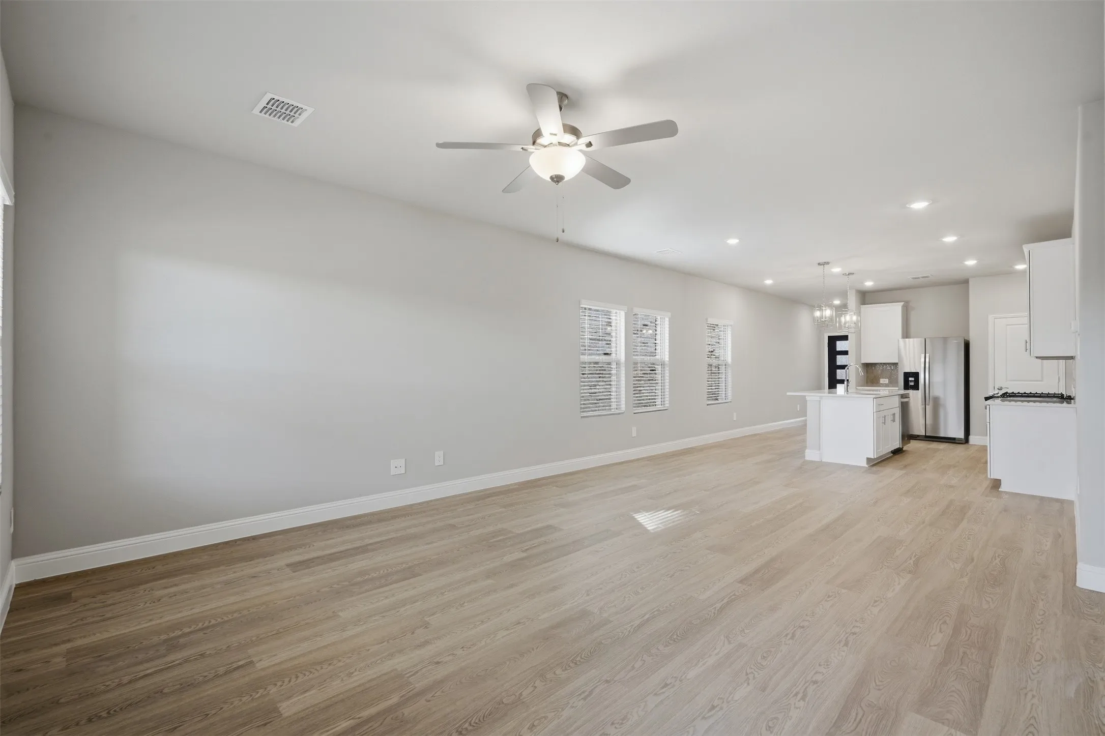 Expansive open-concept living area featuring light wood-finish flooring, recessed lighting, and a ceiling fan