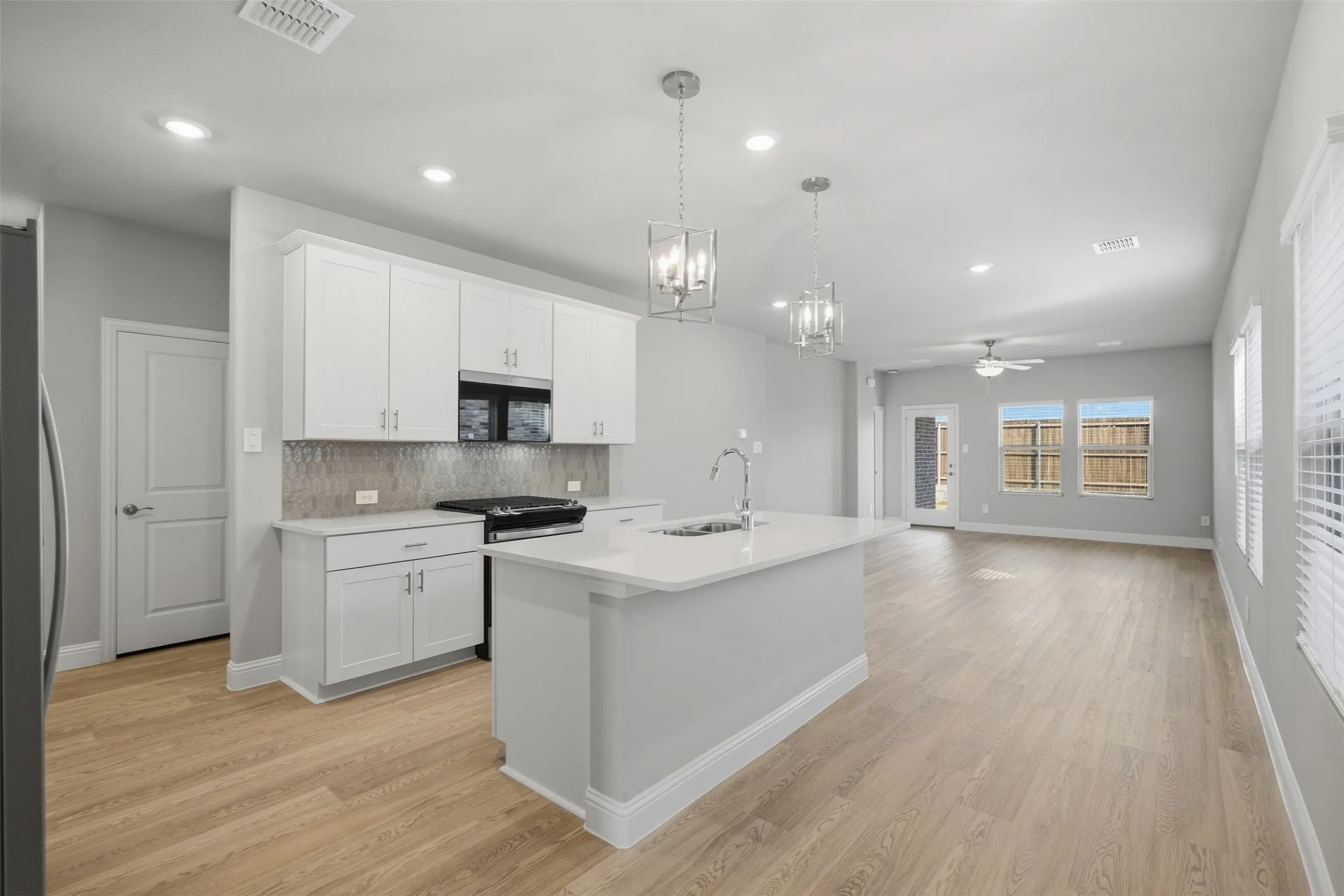 Contemporary kitchen featuring white cabinetry, a central island with a sink, stainless steel appliances, and wood-finish flooring