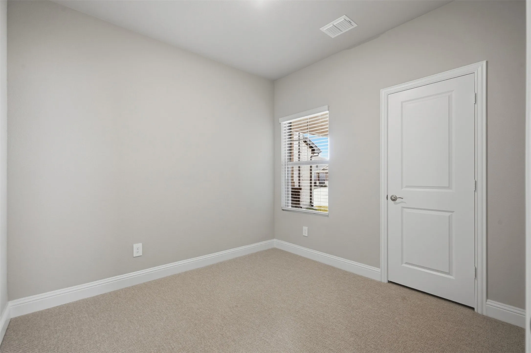 Neutral tone walls, carpet flooring, window with blinds, paneled door with lever hardware, and recessed lighting