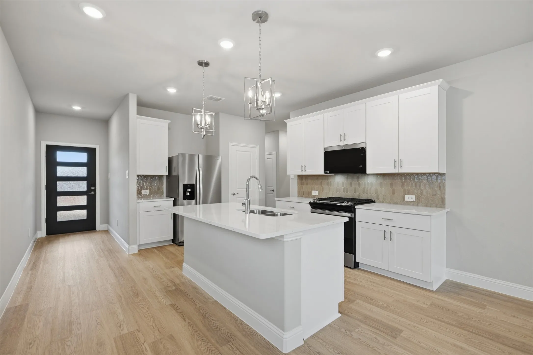 Contemporary kitchen featuring a center island with sink, white shaker cabinetry, stainless steel appliances, and wood-finish flooring