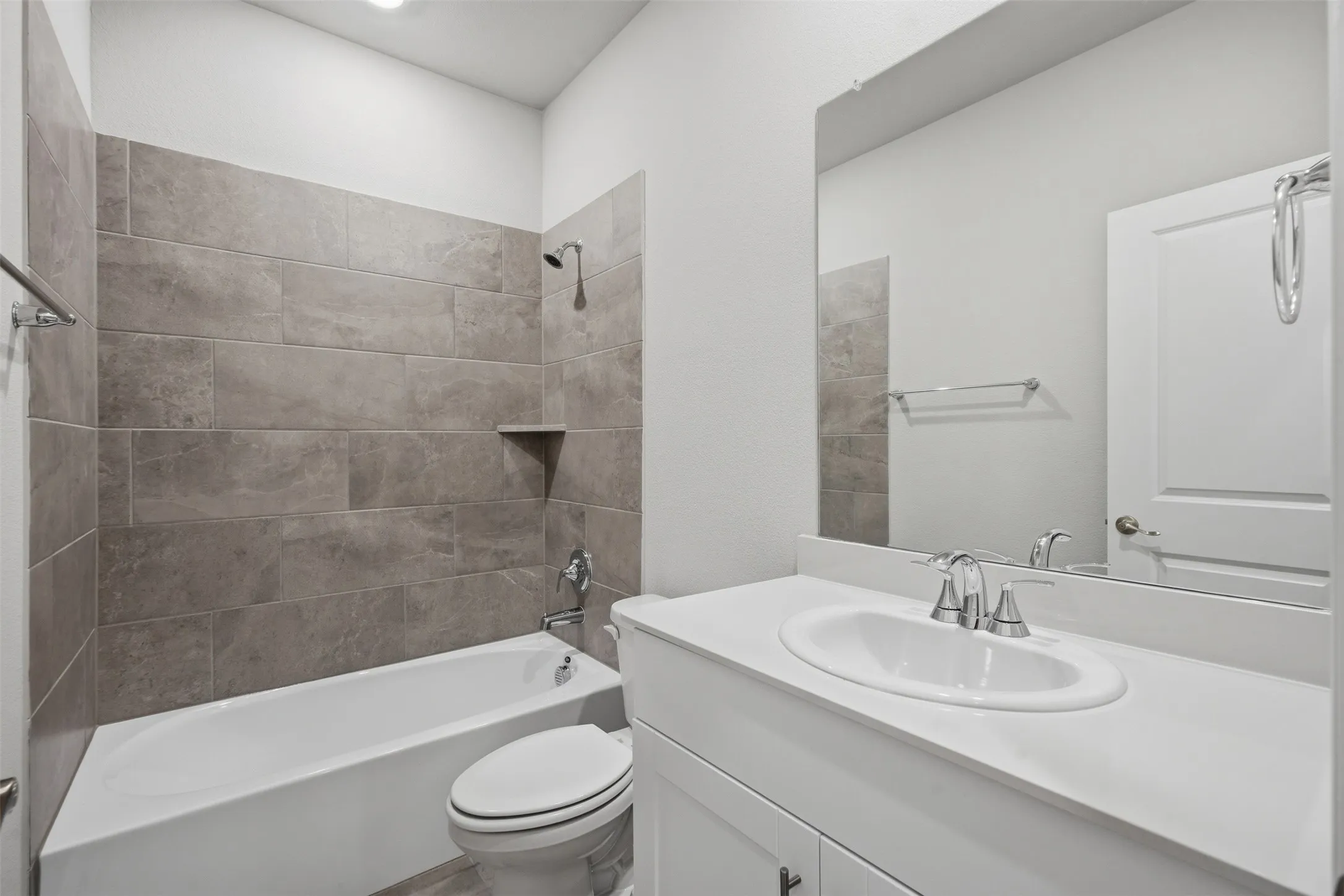 Bathtub with tile surround, built-in shower niche, chrome showerhead, and matching chrome hardware