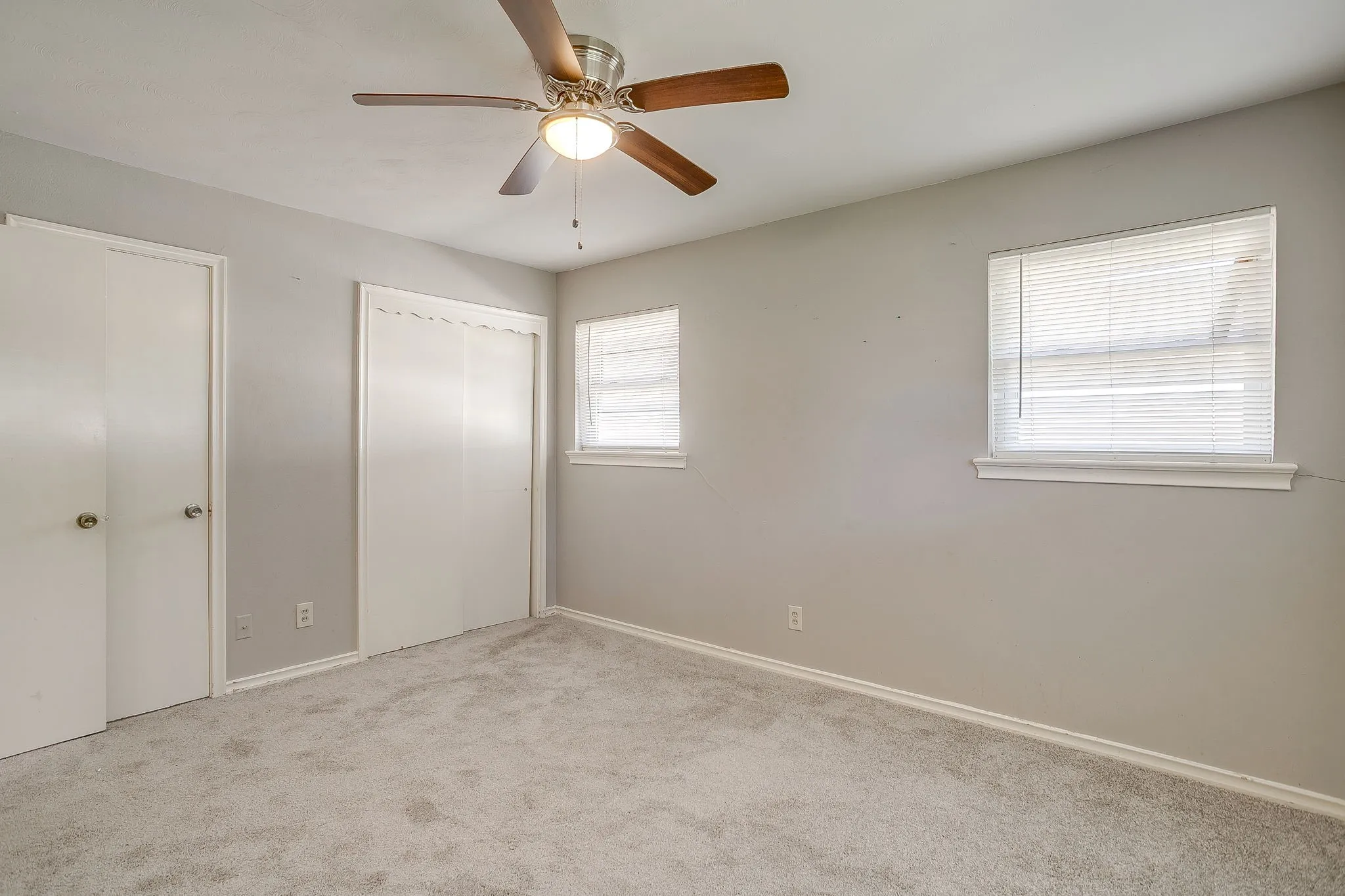 Guest bedroom #1 Plush carpet flooring, neutral wall tones, two windows with blinds, a ceiling fan with integrated lighting, and white trim