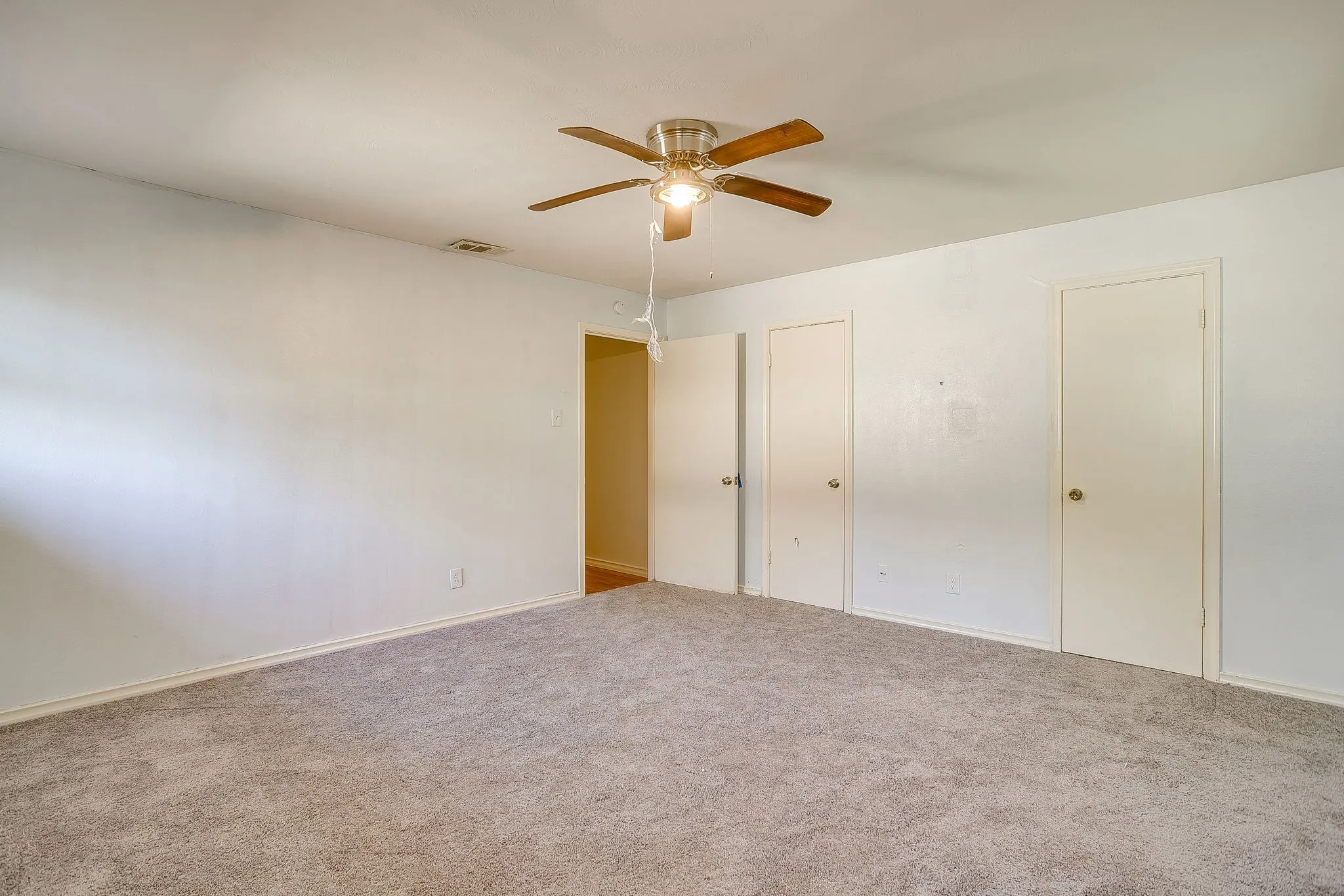 Carpeted room featuring a ceiling fan with light, white walls, and multiple panel doors