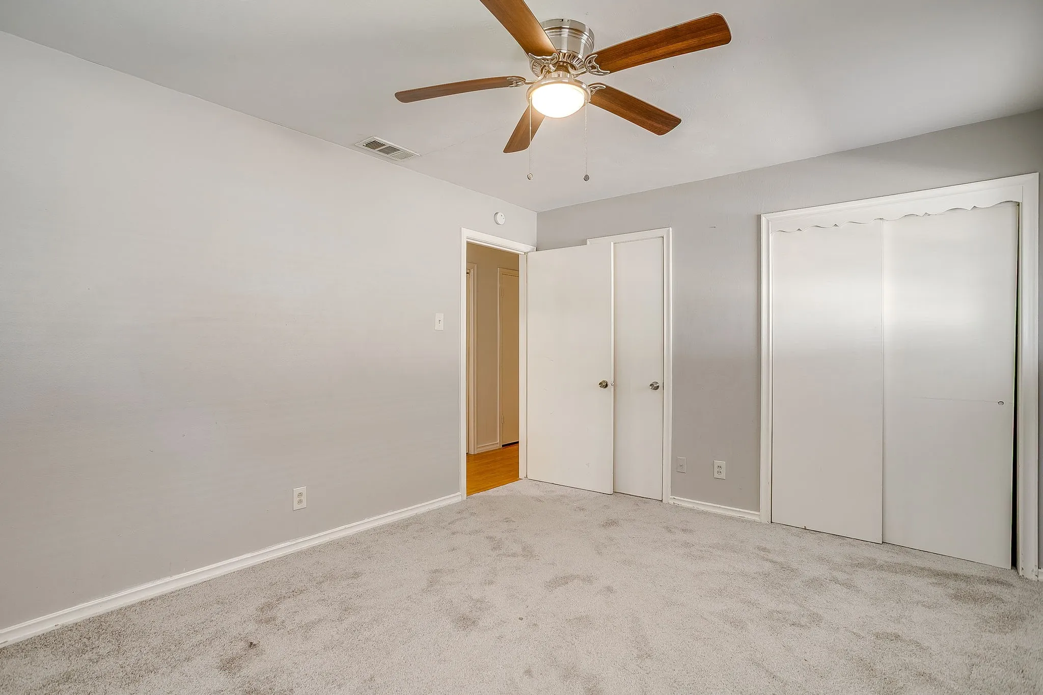 Guest bedroom #1 Light gray wall paint, textured gray carpet, ceiling fan with wood-finish blades, white trim, and white bi-fold closet doors