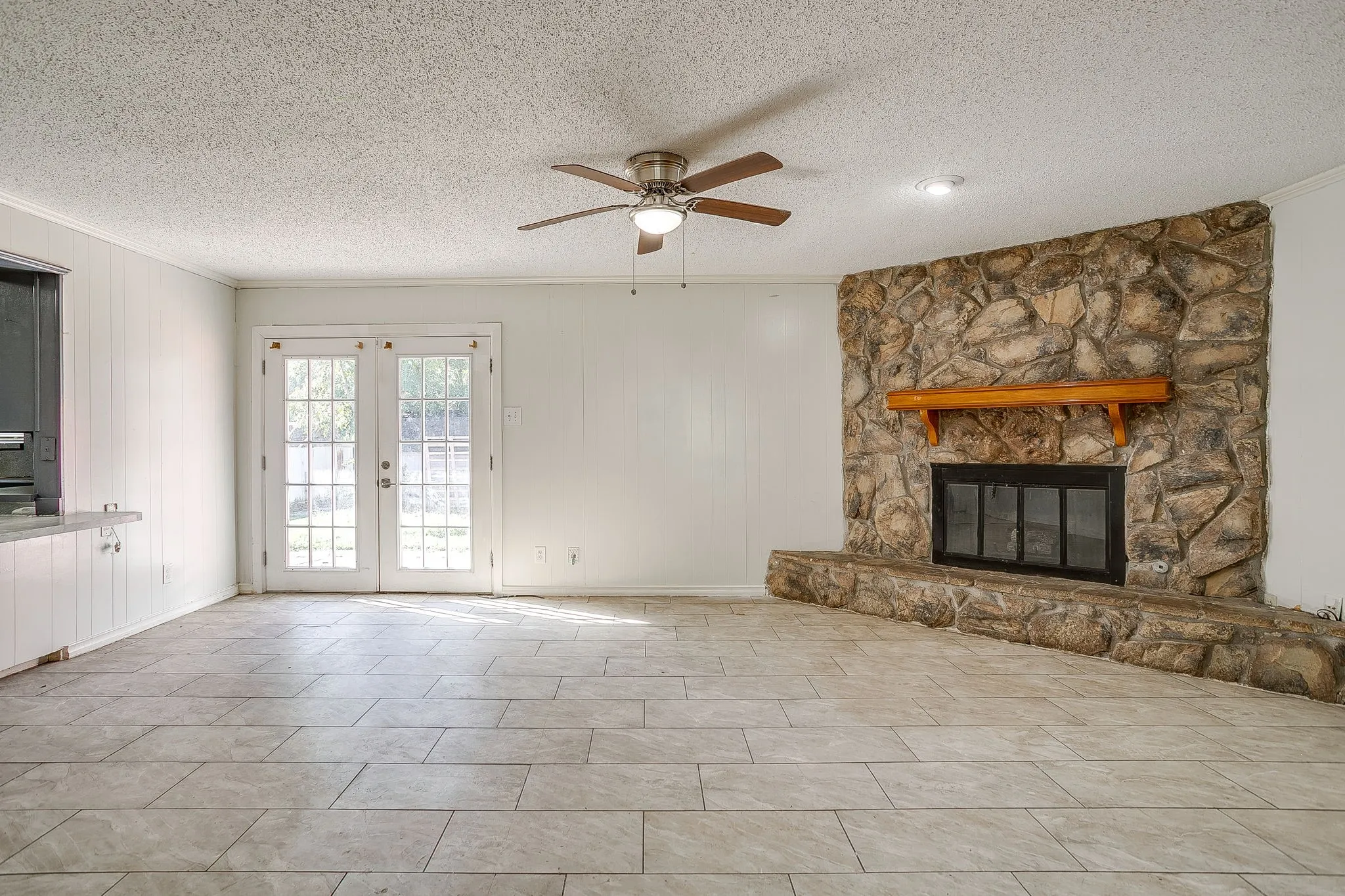 Stone-clad fireplace with a wood mantle, tile flooring, ceiling fan, recessed lighting, and double glass-paneled doors