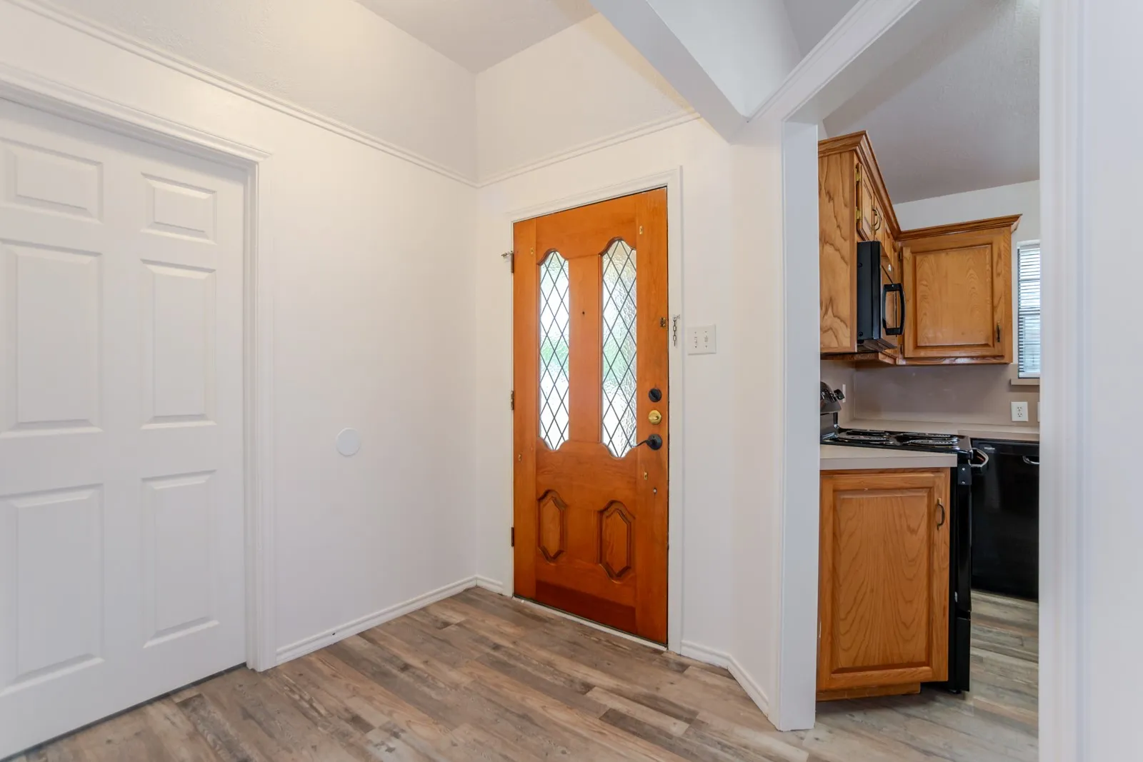Wood-finish flooring, paneled entry door with leaded glass insert, and white trim throughout