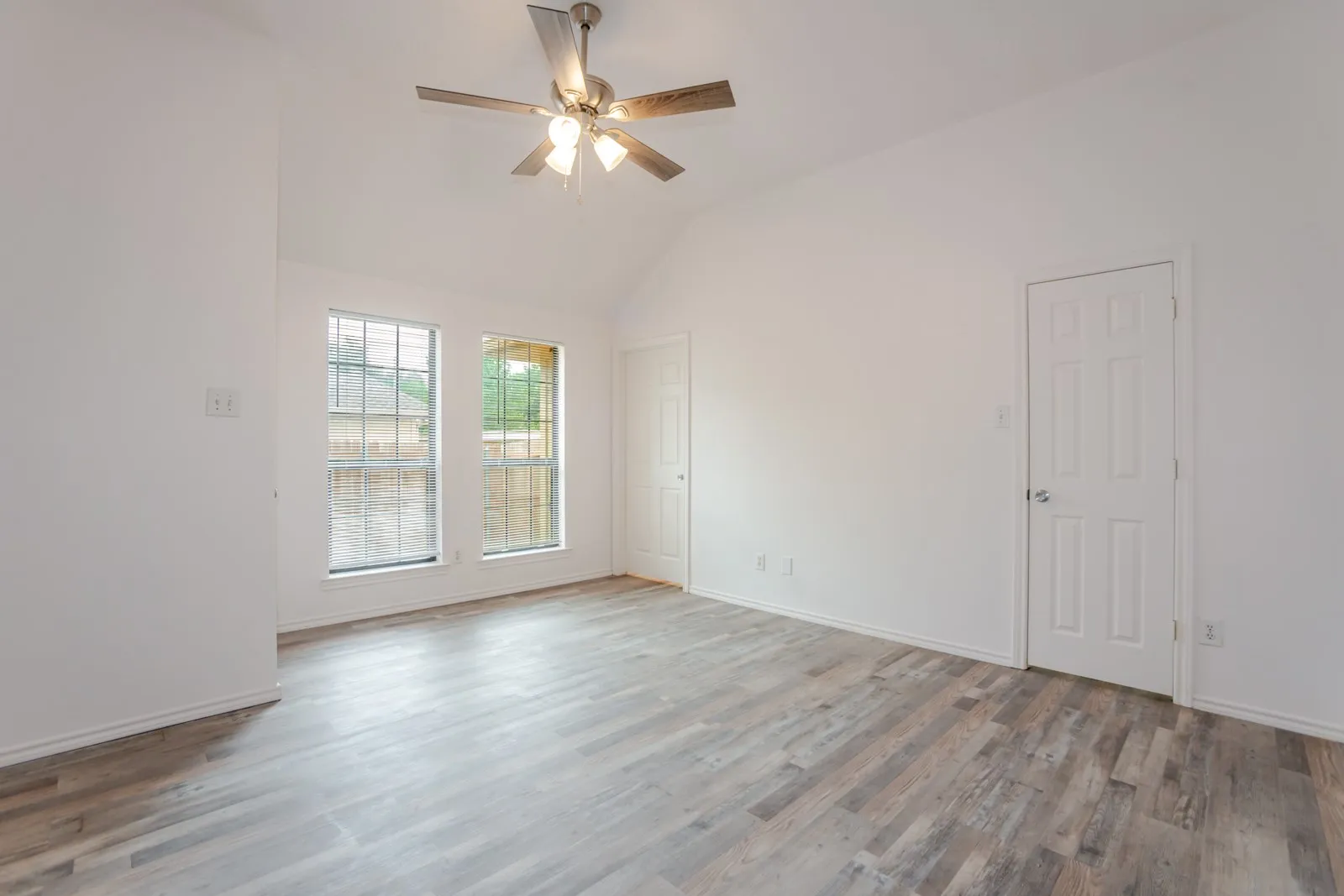 Vaulted ceiling with a ceiling fan, two windows, wood-finish flooring, and white paneled doors