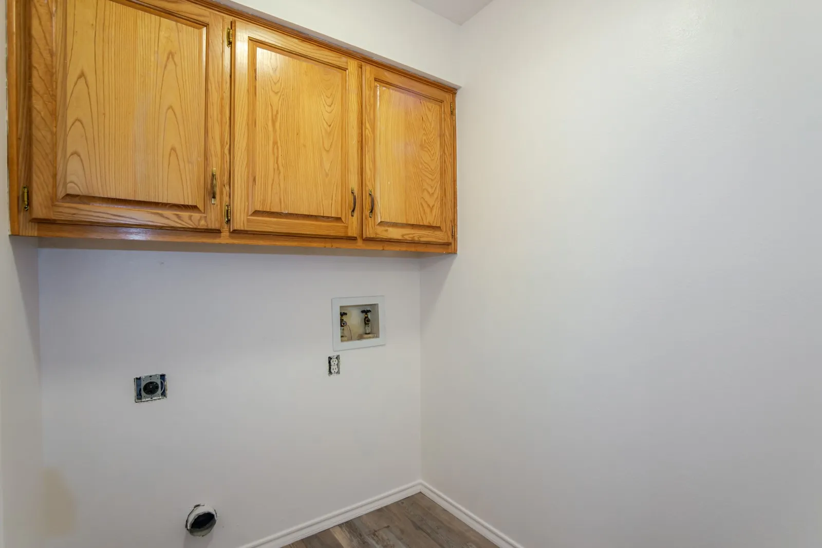 Wood-finish overhead cabinetry, wood-finish flooring, and white walls