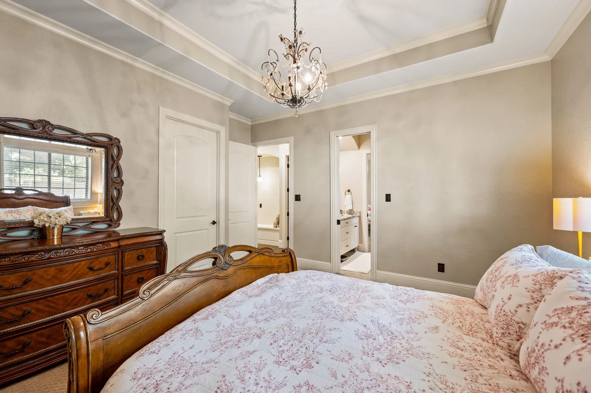 Tray ceiling with crown molding, decorative chandelier, light-toned wall finish, white interior doors, and a window with exterior views