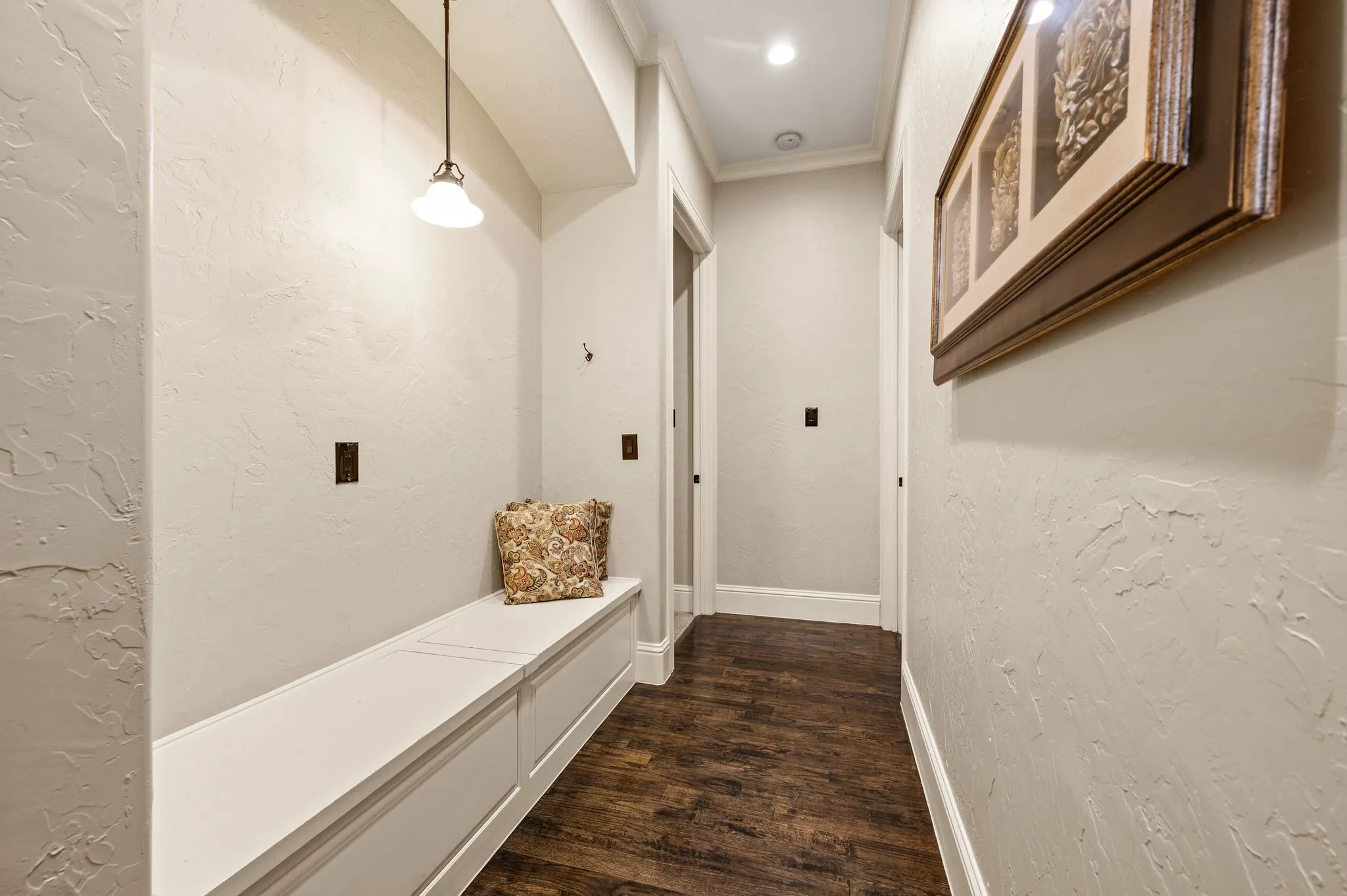 Built-in storage bench, wood-finish flooring, textured wall finish, and crown molding