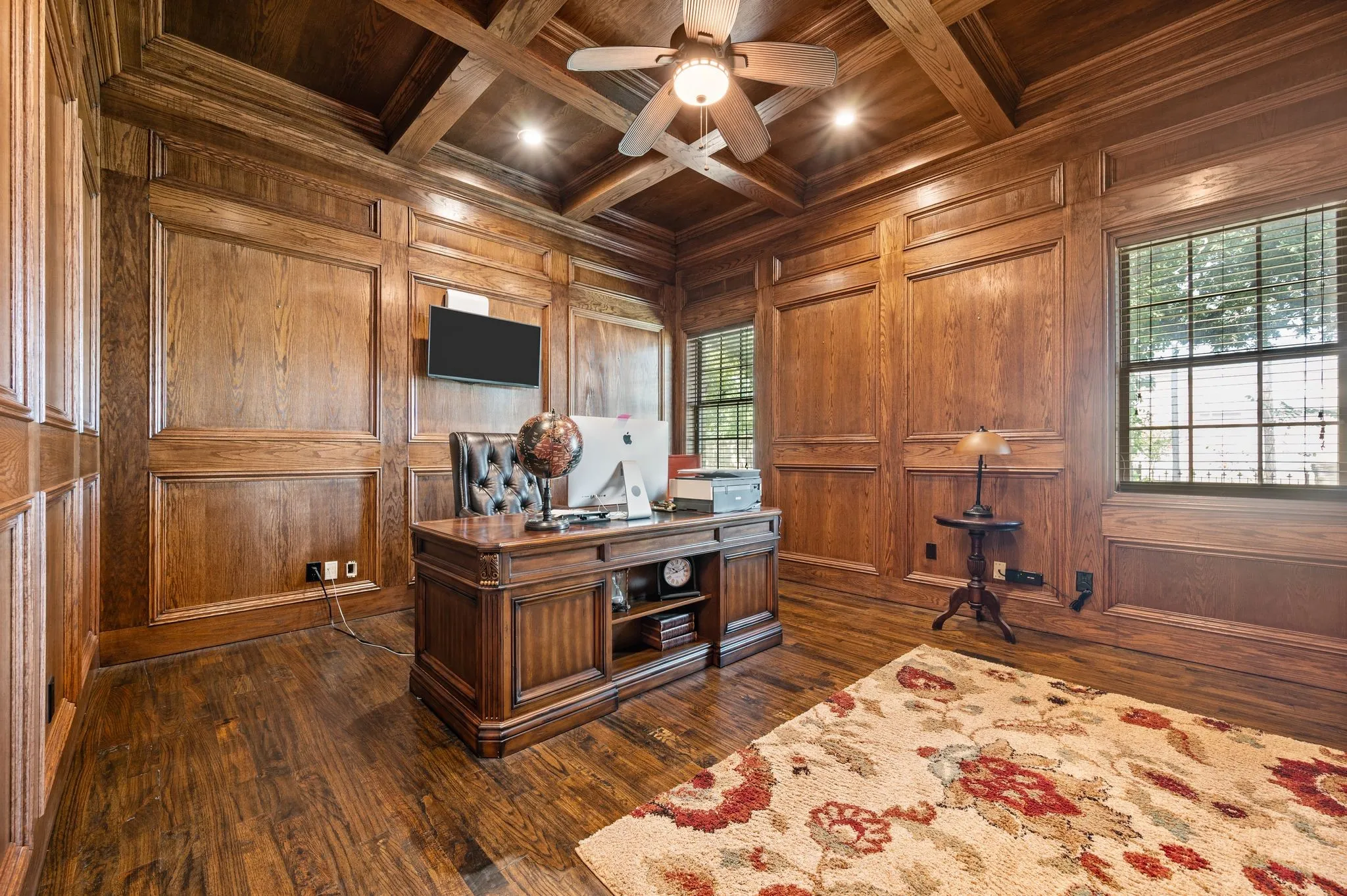 Dark wood-paneled walls, wood-finish flooring, coffered ceiling with recessed lighting, and multiple windows
