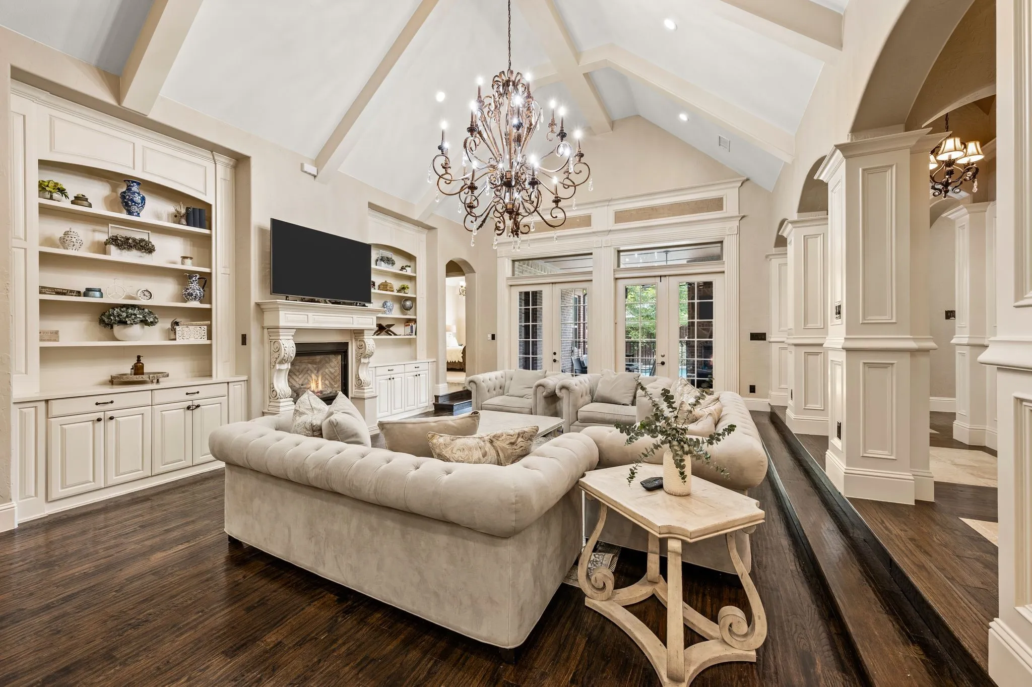 Vaulted ceiling with exposed beams, wood-finish flooring, built-in cabinetry, a decorative fireplace, and French doors