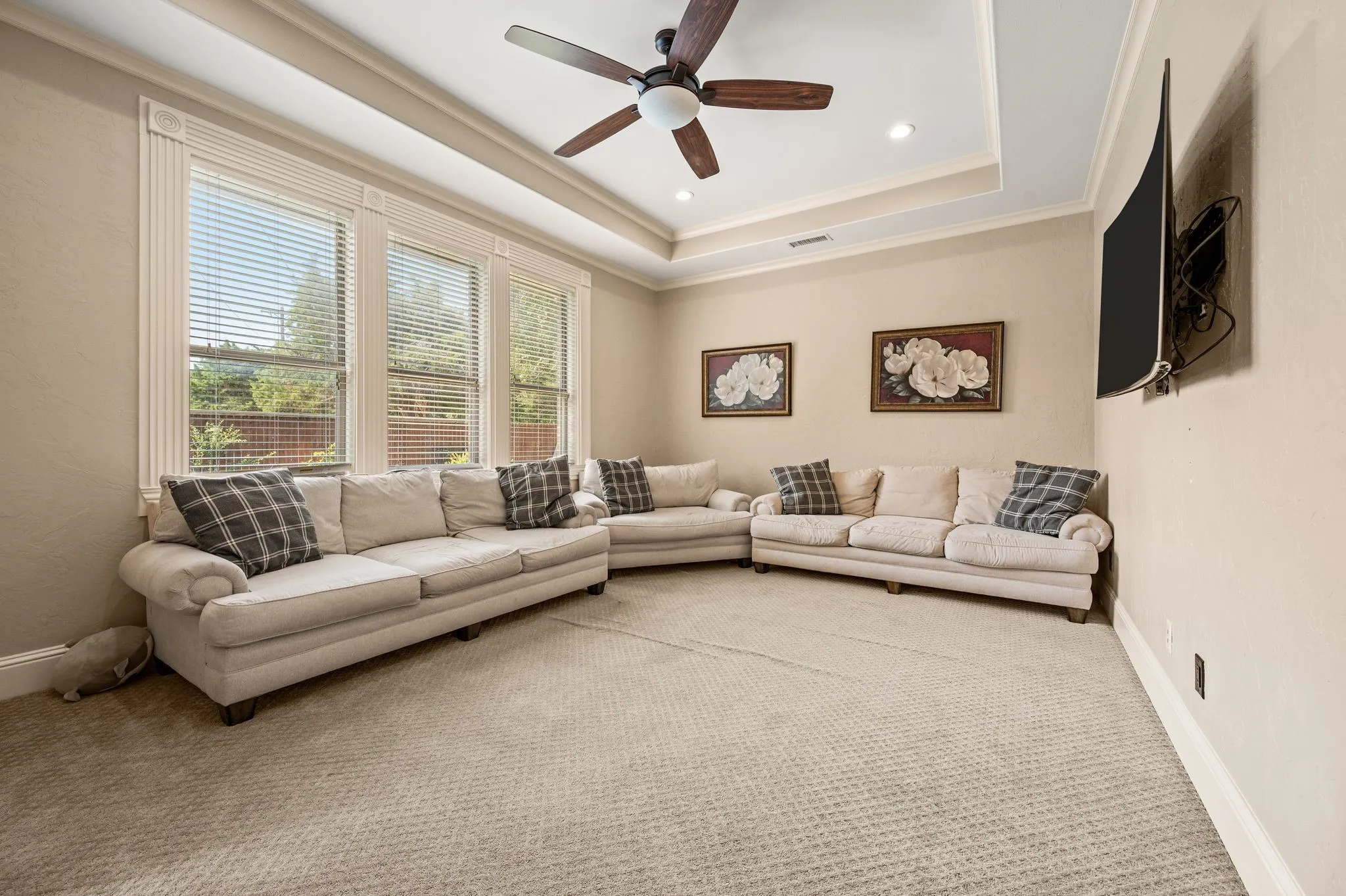 Tray ceiling with a ceiling fan, recessed lighting, expansive window bank with blinds, and wall-mounted television bracket