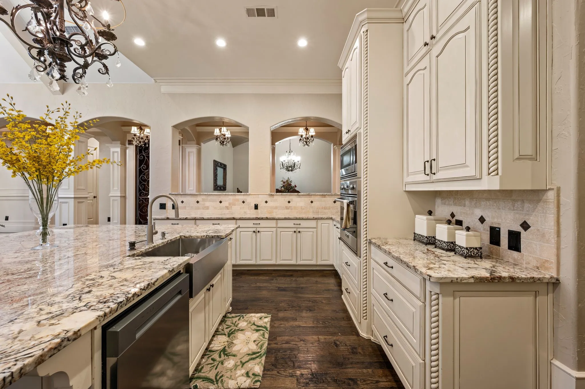 Cream cabinetry with rope molding details, stone countertops, stainless steel apron-front sink, integrated stainless steel appliances, and dark wood-finish flooring
