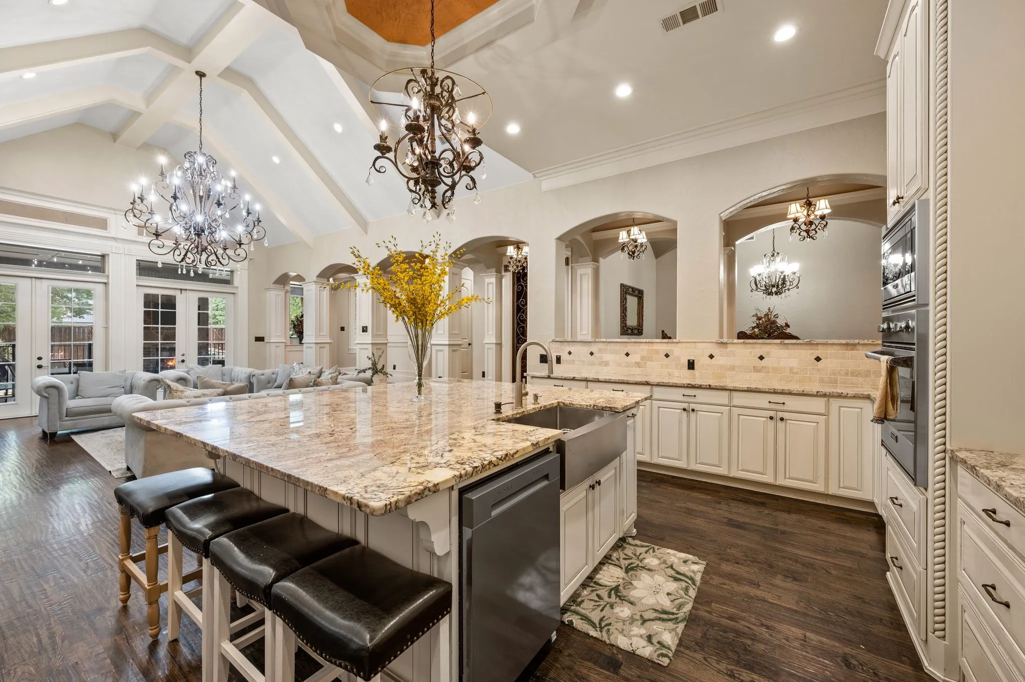 Kitchen featuring a large central island with seating, dark wood-finish flooring, white cabinetry, integrated stainless-steel appliances, and arched doorways