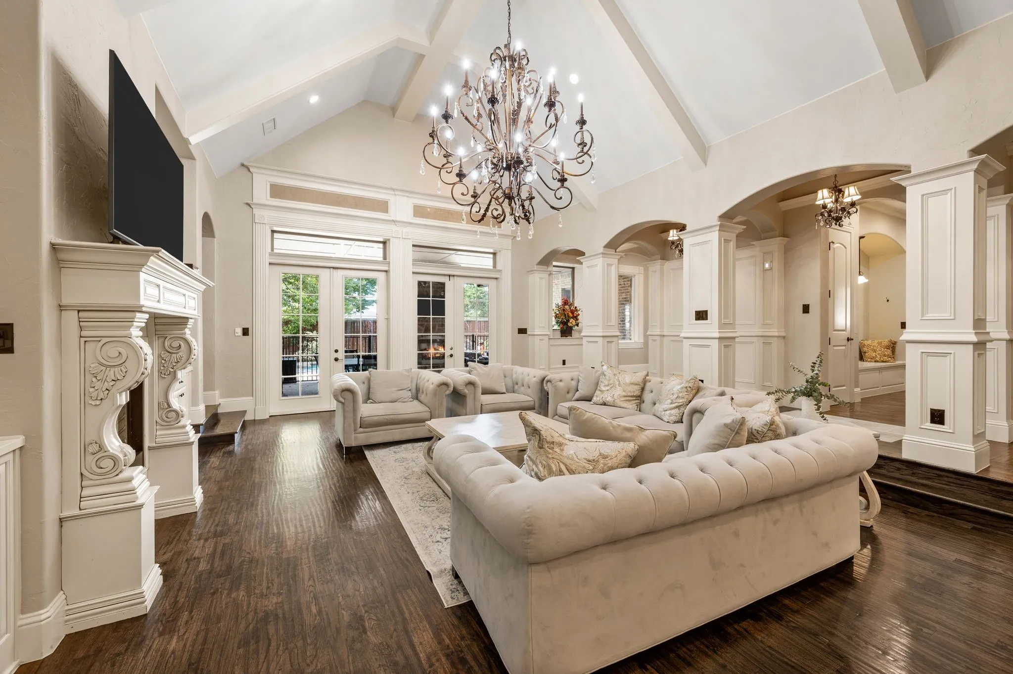 Vaulted ceiling with exposed beams, decorative chandelier, wood-finish flooring, architectural columns, and French doors