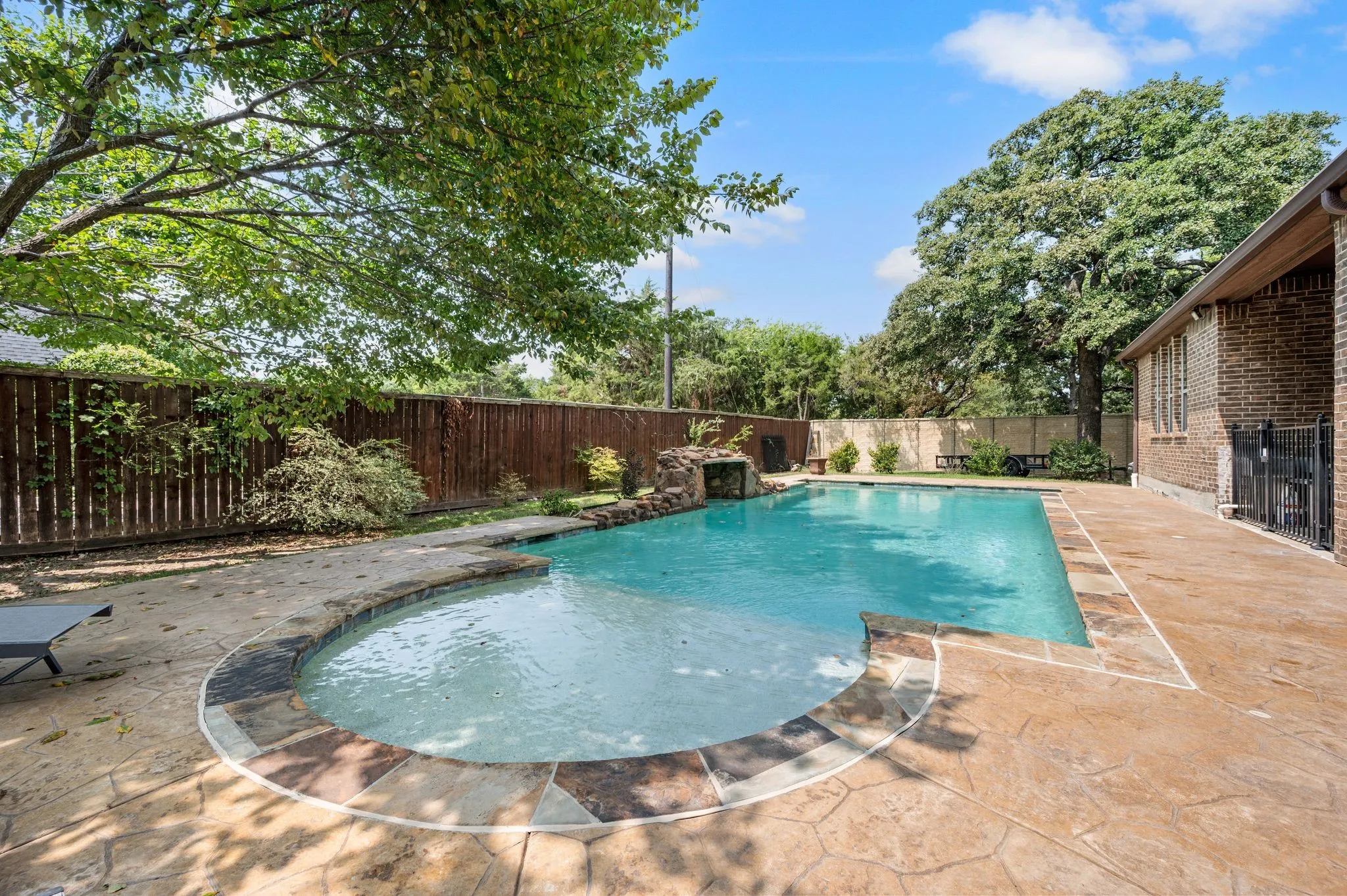 Resort-style swimming pool featuring a curved design with integrated sun shelf, surrounded by stamped concrete decking