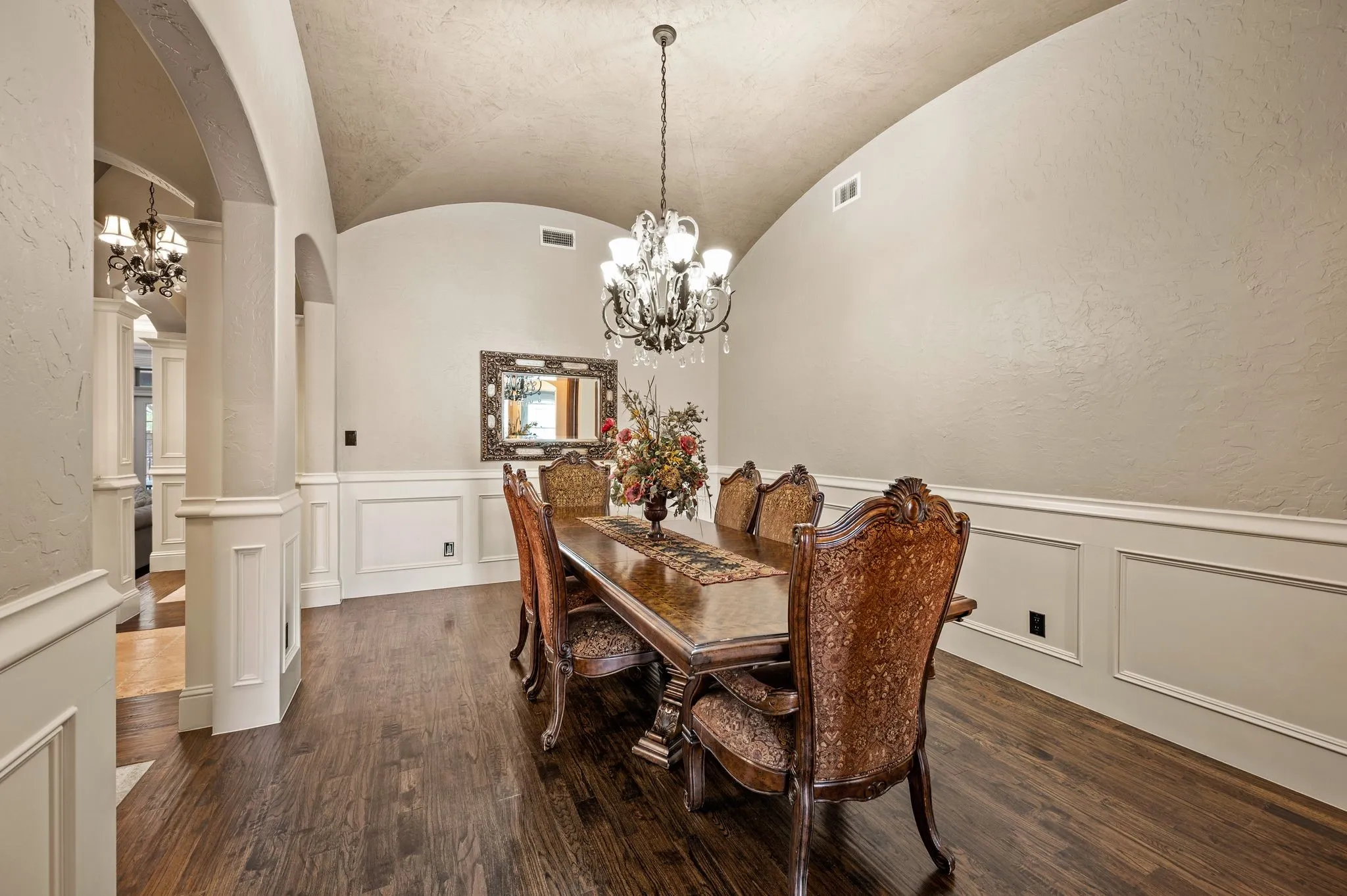 Arched entryway with decorative columns, barrel-vaulted ceiling, dark wood-finish flooring, white wainscoting, and an ornate chandelier