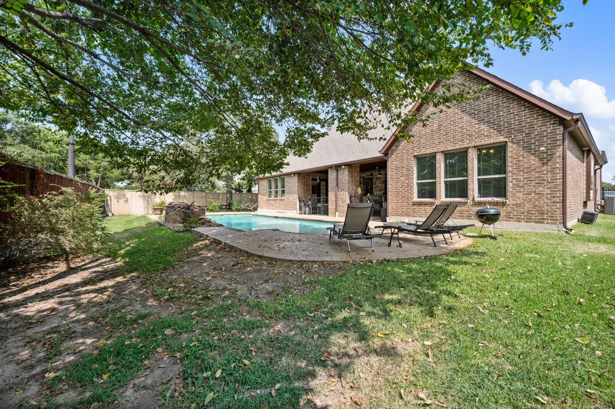 Brick exterior with multiple windows, concrete patio, inground pool, and fenced perimeter