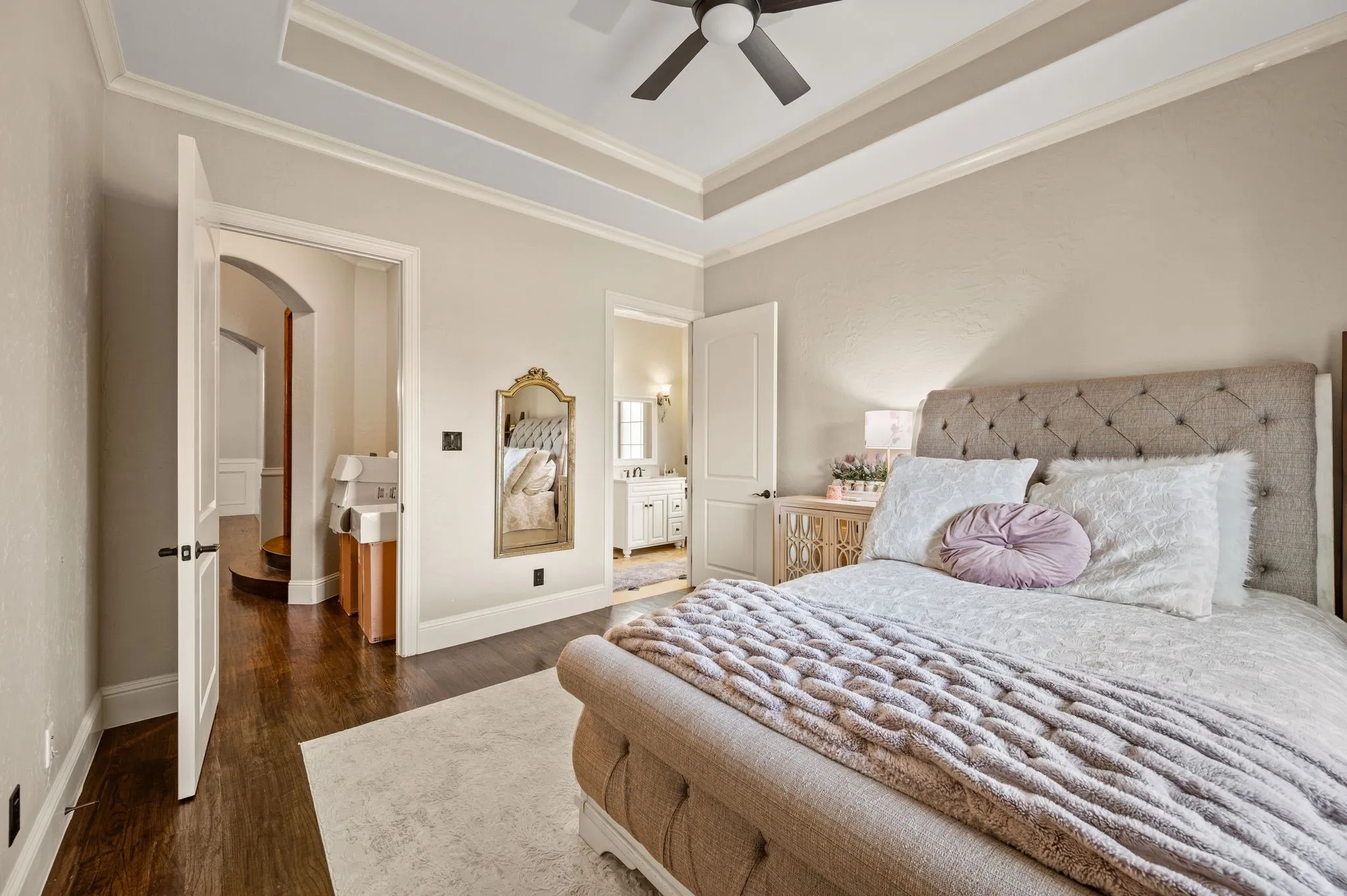 Tray ceiling with crown molding, wood-finish flooring, ceiling fan, and arched entryway