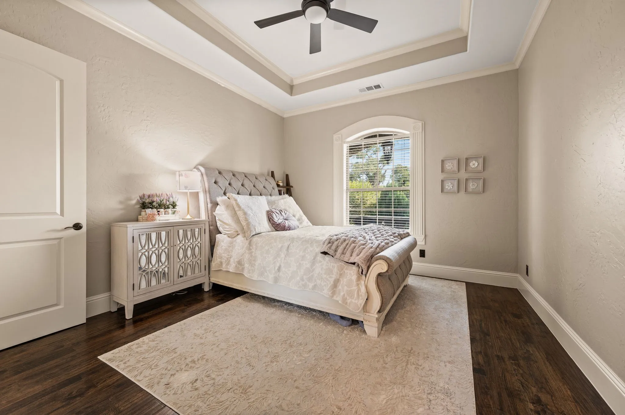 Tray ceiling with crown molding, ceiling fan, arched window, and wood-finish flooring