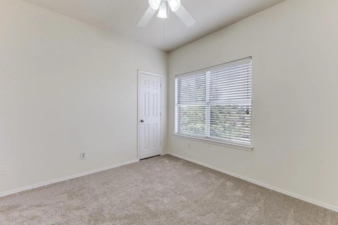 Neutral wall paint, carpet flooring, a multi-panel door, and a ceiling fan with integrated lighting
