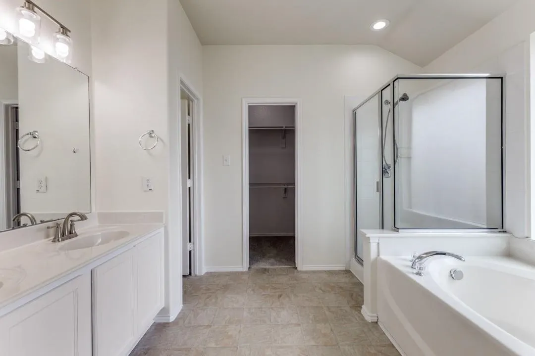Dual vanity with undermount sinks, a built-in soaking tub, a separate glass-enclosed shower, and a walk-in closet