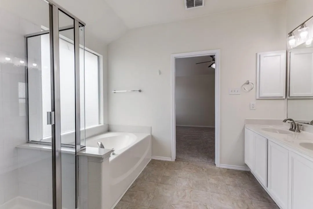 Dual vanity with undermount sinks, separate soaking tub, glass-enclosed shower, and vinyl flooring