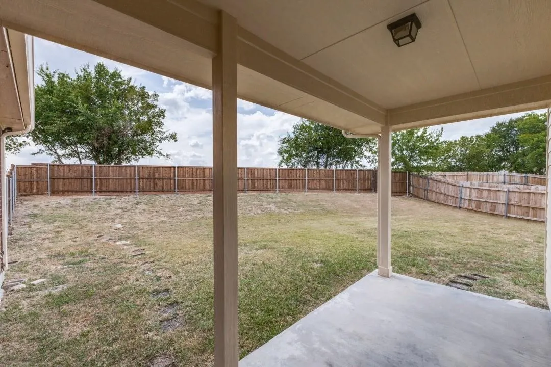 Covered concrete patio, expansive grassy yard, and full privacy fencing