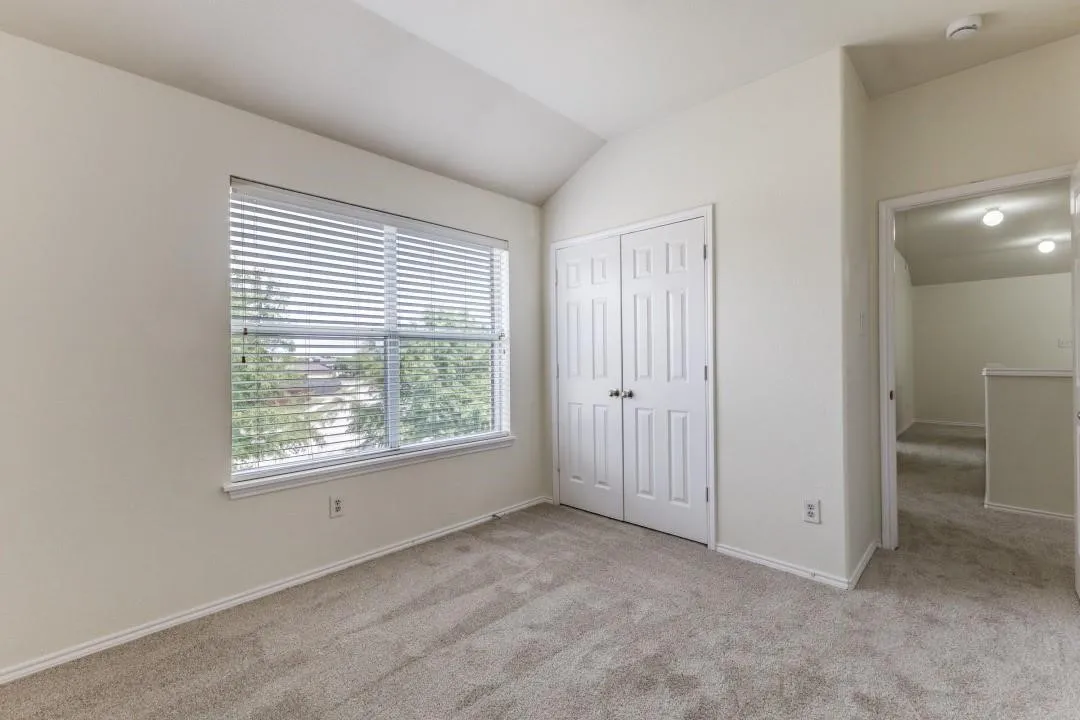 Window with horizontal blinds, neutral wall paint, light-colored carpeting, white paneled bifold closet doors, vaulted ceiling