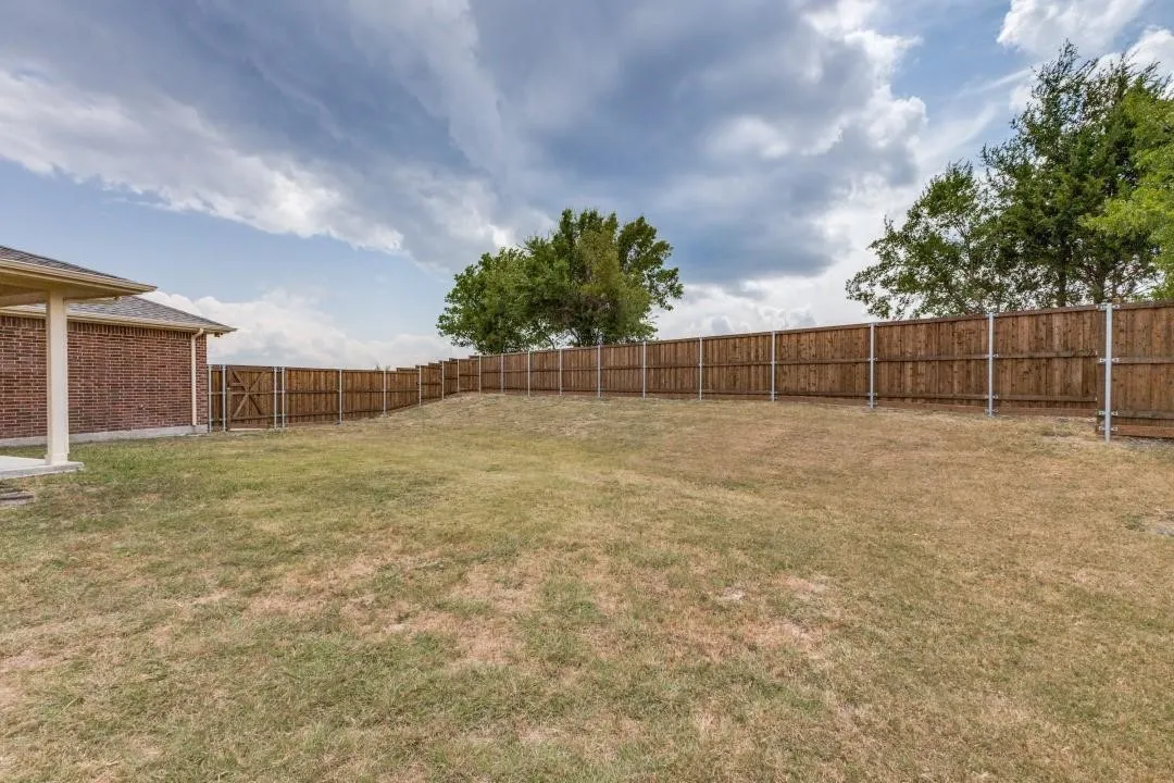 Expansive backyard with a full wood privacy fence and a brick-sided structure featuring a covered patio