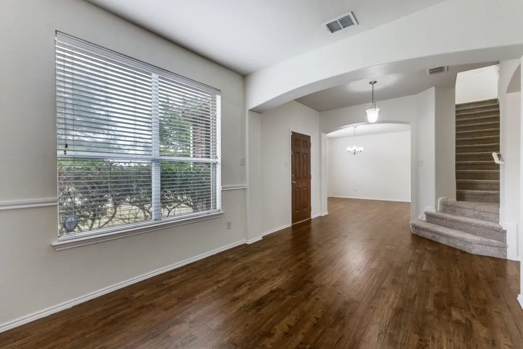 Wood-finish flooring, large window with blinds, archways, pendant lighting, and carpeted stairs