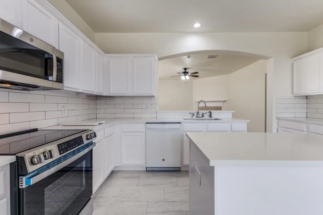 White cabinetry with brushed nickel hardware, subway tile backsplash, stainless steel microwave, and built-in electric range