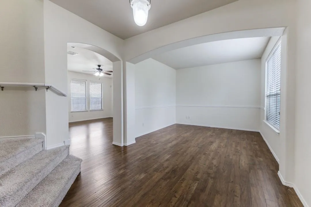 Hardwood-finish flooring, arched entryway, ceiling-mounted light fixture, carpeted staircase with handrail, and window with blinds