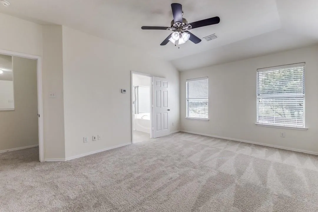 Spacious room featuring vaulted ceilings, carpeted flooring, a ceiling fan, and two windows with blinds