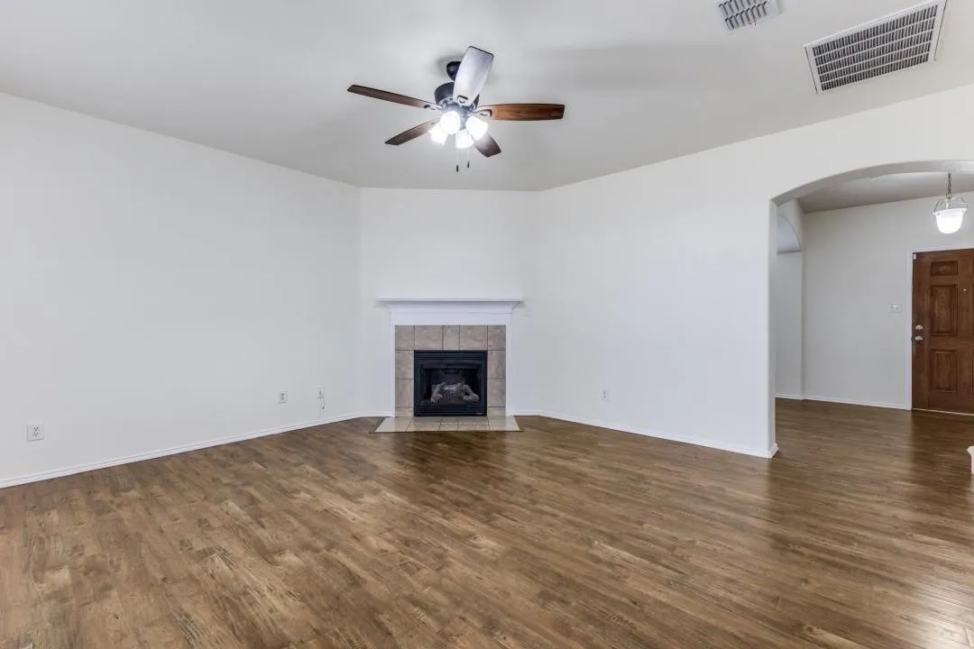 Wood-finish flooring, tiled fireplace with mantel, ceiling fan with integrated lighting, and an arched entryway