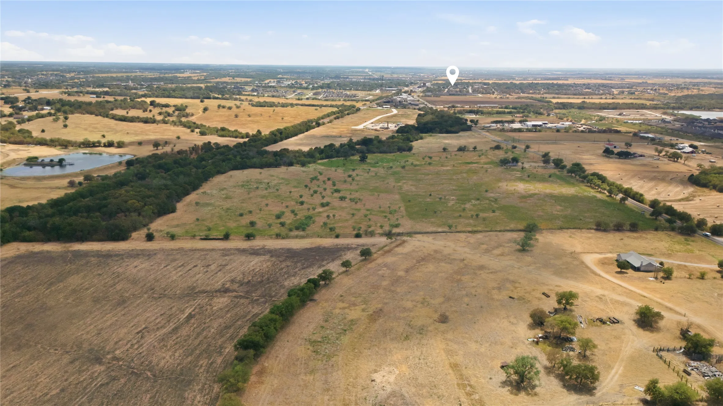 Expansive acreage featuring a natural pond, wooded areas, and open fields with surrounding infrastructure