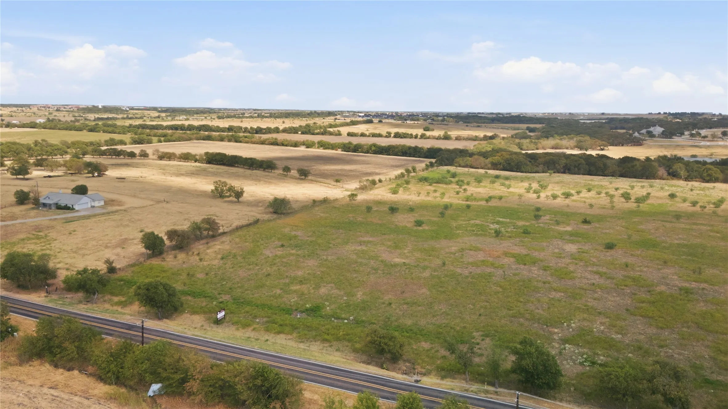 Expansive rural landscape featuring scattered trees, open fields, and a distant residential​​‌​​​​‌​​‌‌​‌‌​​​‌‌​‌​‌​‌​​​‌​​ structure