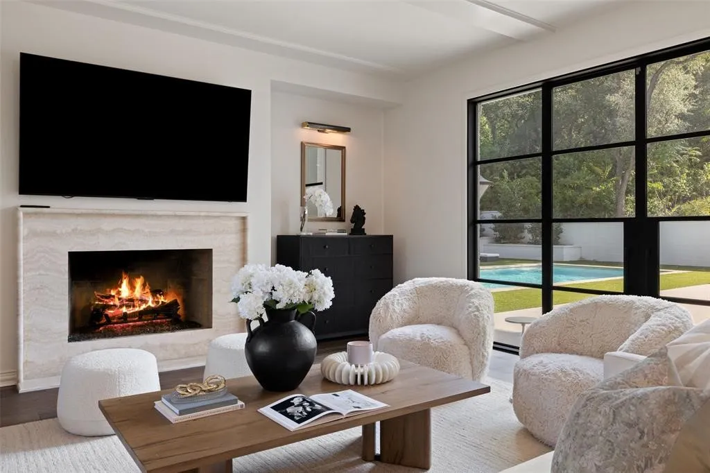 Travertine surround fireplace, dark wood-finish flooring, metal-framed window, built-in cabinetry, and integrated ceiling lighting