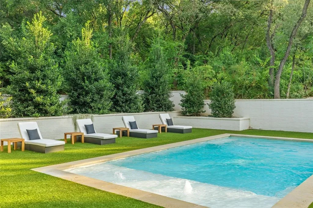 Rectangular swimming pool with integrated spa, bordered by artificial turf and a white block wall