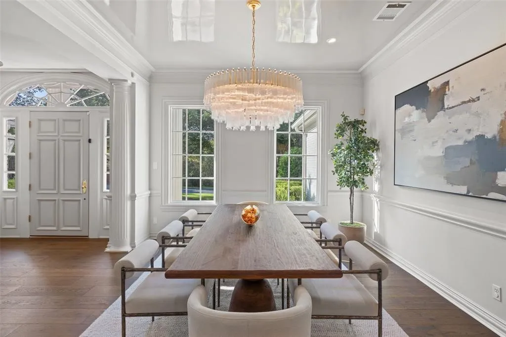 Hardwood flooring, custom millwork, large windows, elegant chandelier, and a paneled entry door with transom window