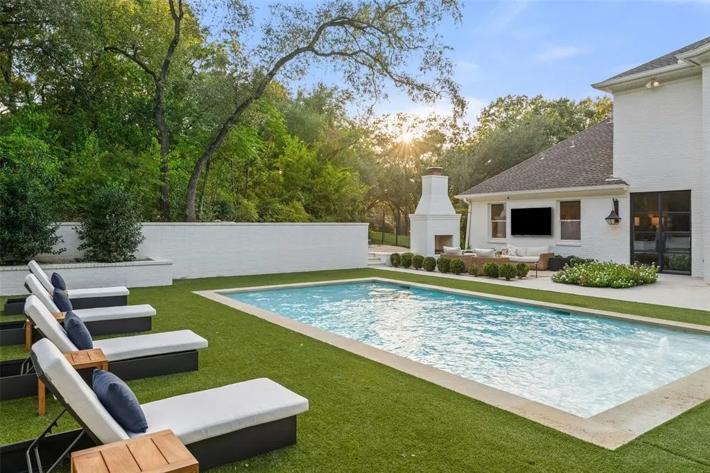 Outdoor living area featuring a rectangular swimming pool, artificial turf surround, an outdoor fireplace, and a white brick exterior