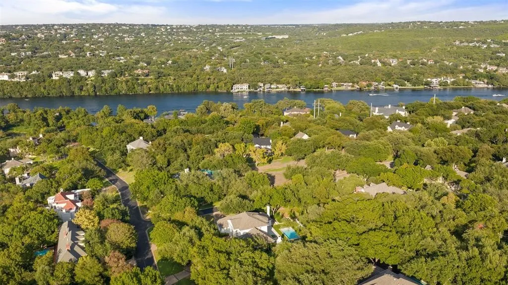 Residential area surrounded by mature trees, featuring a river and hills in the background