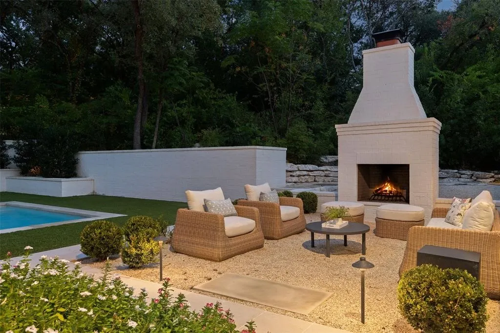 Expansive outdoor living area featuring a prominent brick fireplace, a manicured lawn, and a swimming pool