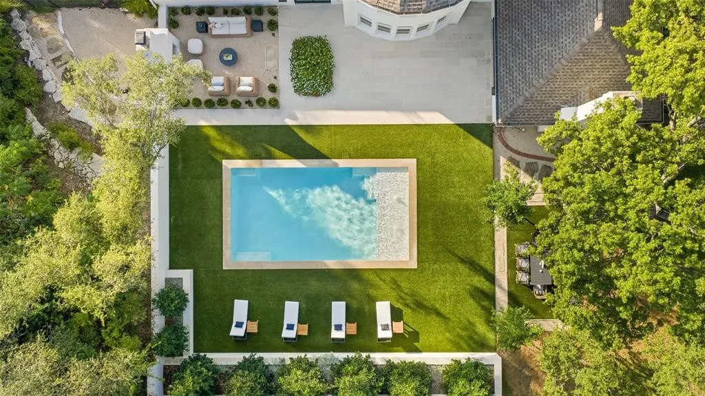 Expansive backyard featuring a rectangular swimming pool, surrounding green lawn, and multiple paved patio areas