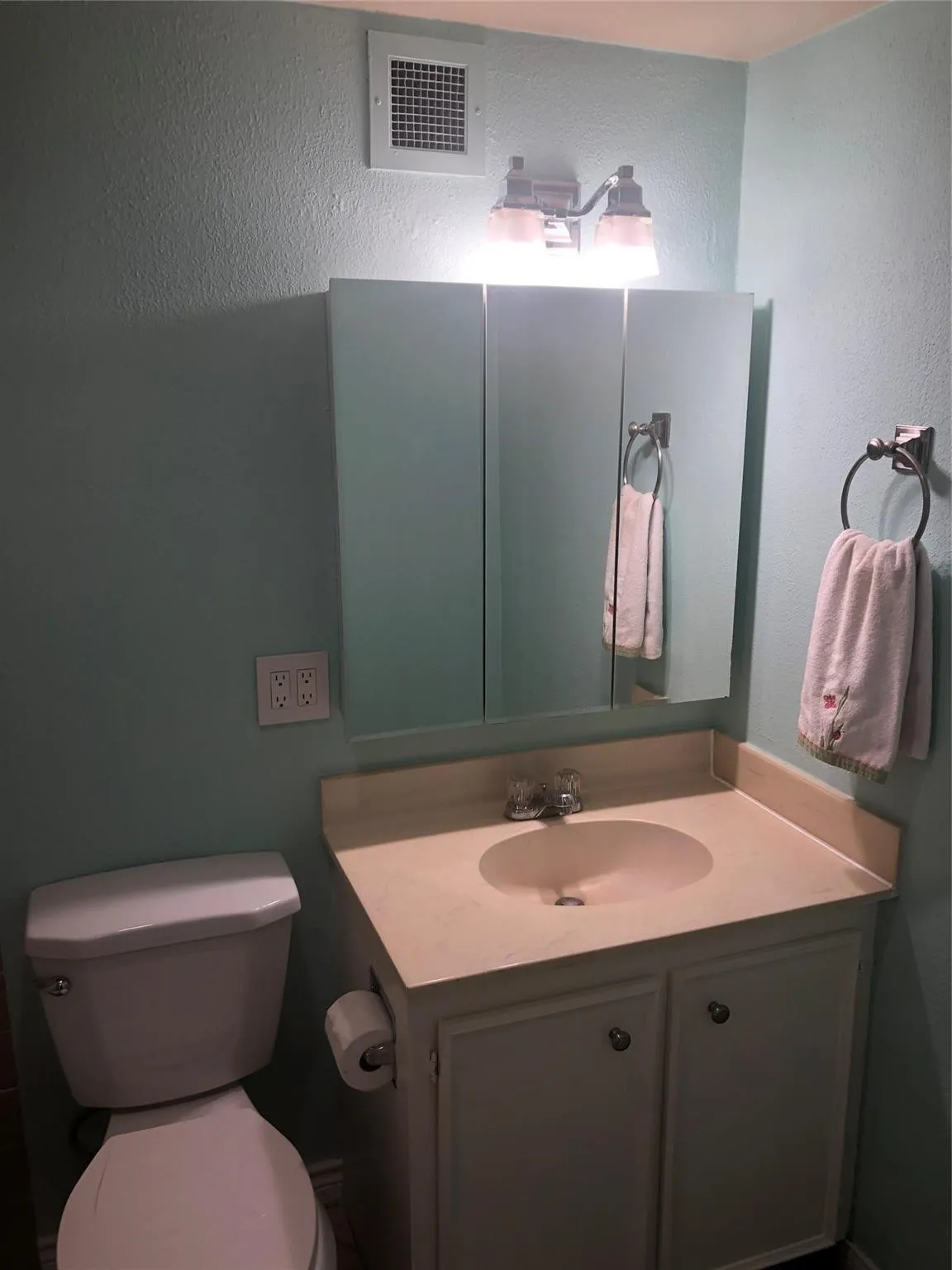 Vanity with integrated sink and storage cabinetry, tri-fold mirrored medicine cabinet, and wall-mounted lighting fixture