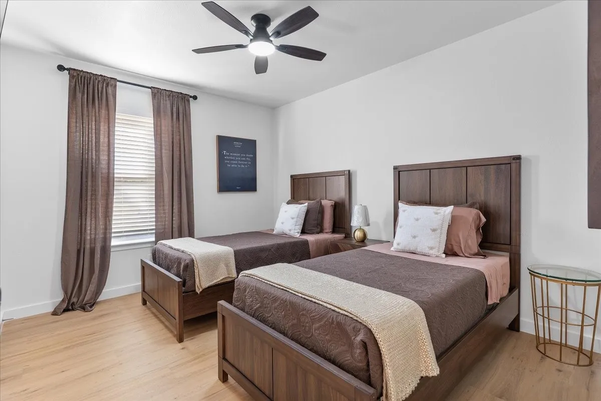 Light wood-finish flooring, a window with horizontal blinds, and a ceiling fan with integrated lighting