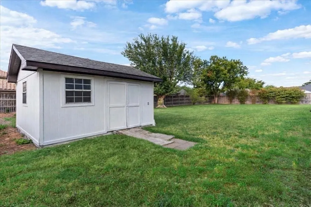 Expansive grassy yard with a white storage shed featuring a shingled roof and multiple windows